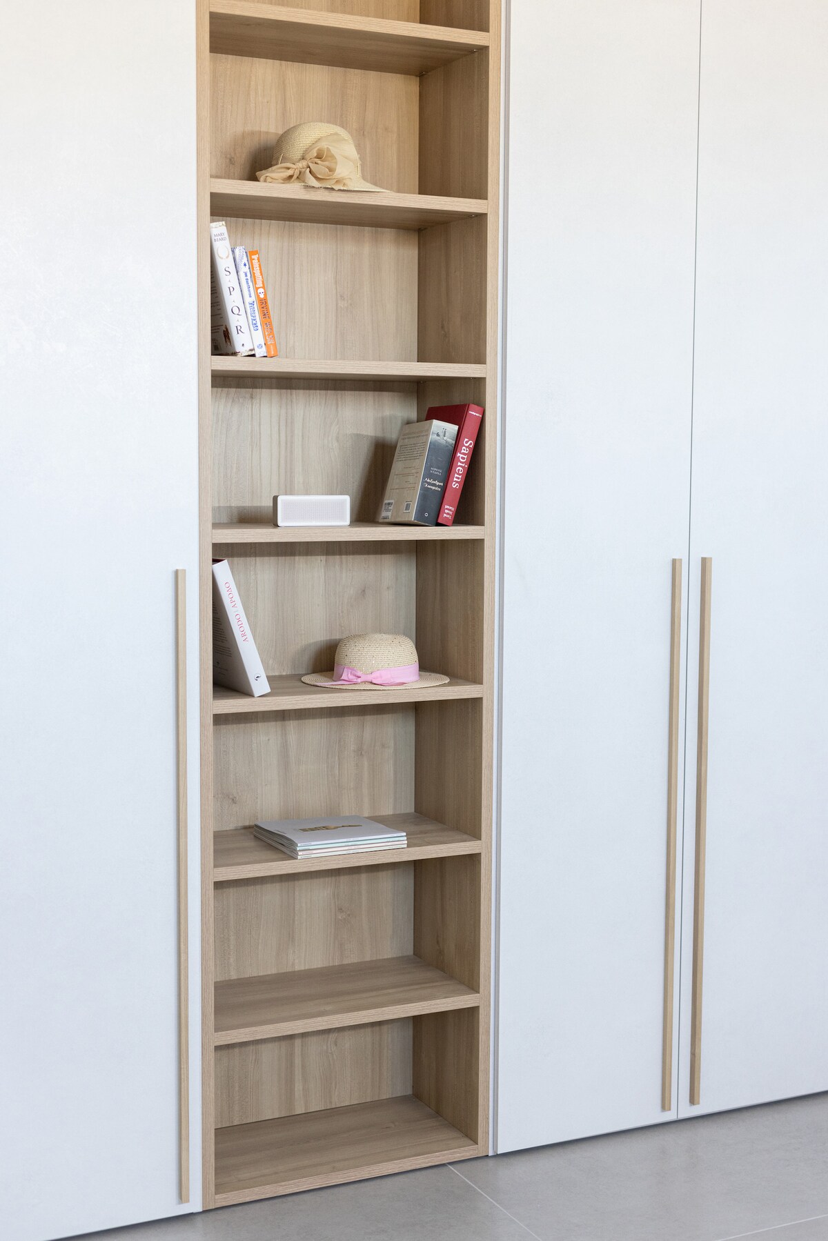 A wooden shelving unit features several neatly arranged books, along with decorative items such as a small hat and a decorative box. The shelves are framed by white cabinetry, providing a clean and organized appearance.
