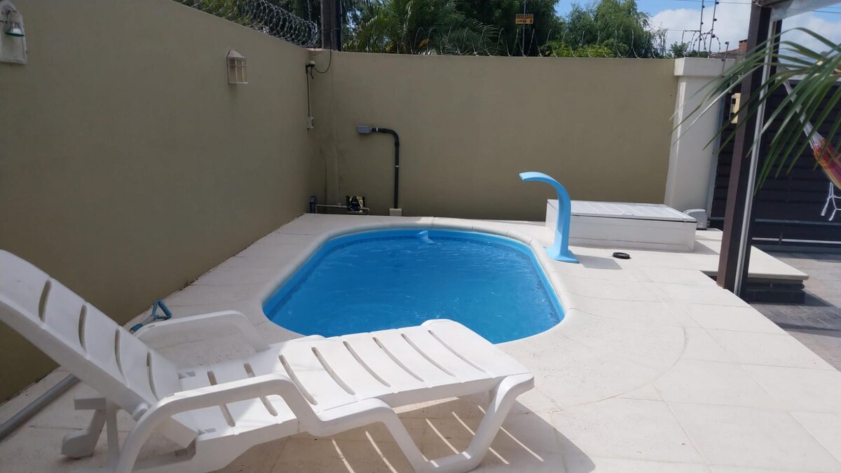 A private pool area is surrounded by a minimalistic patio, featuring a clear blue pool and two white lounge chairs positioned for relaxation. Nearby, a small slide is seen at one end of the pool, providing additional fun.