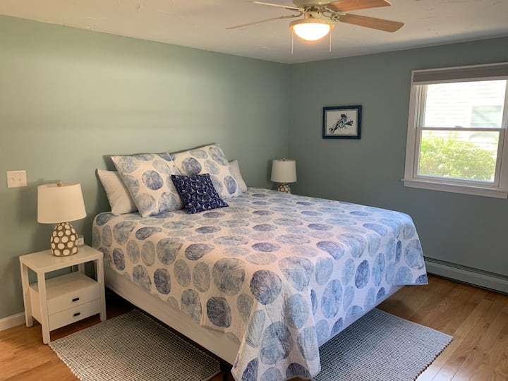 Chumba cha kulala cha msingi kilicho na kitanda cha ukubwa wa kifalme na bafu kuu lililoambatishwa linatazama ua wa nyuma ili iwe tulivu