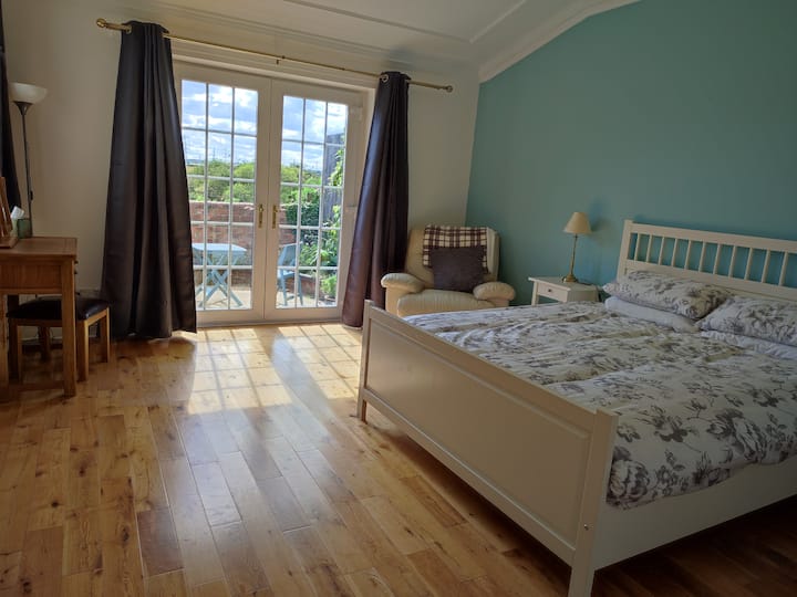 غرفة نوم رئيسية بسرير بمقاس كبير. أبواب الفناء إلى فناء خاص تطل على الحقول.