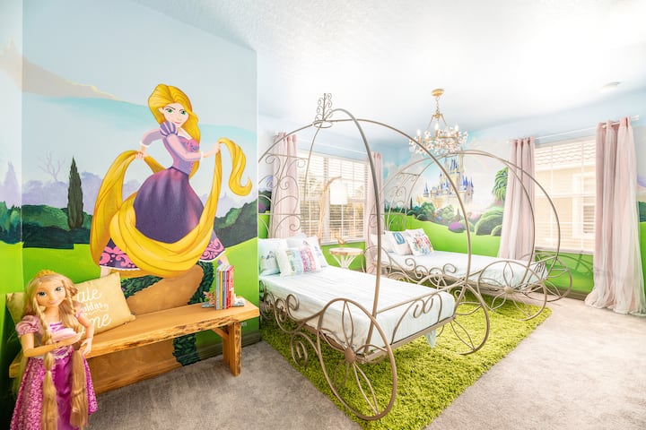 Elegante dormitorio con temática princesa con camas estilo carruaje, un vibrante mural con Rapunzel y un castillo mágico, y toques elegantes como una lámpara de araña. Perfecto para crear recuerdos encantadores en un retiro inspirado en un cuento de hadas.