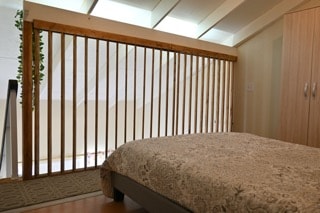 A spacious sleeping area is highlighted by a patterned bedspread covering the bed. Wood railing creates a partial barrier, allowing light to filter into the room. The muted tones of the decor contribute to a calm and inviting environment.