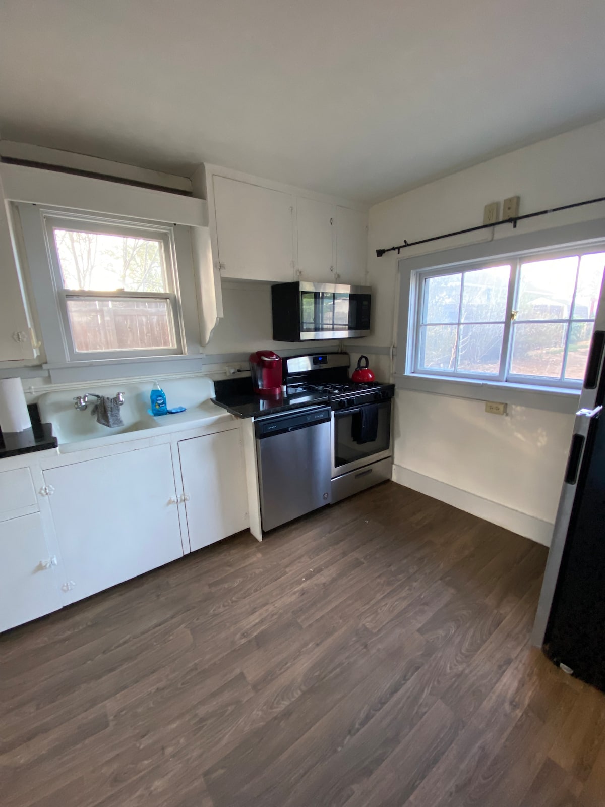 A functional kitchen setup features modern appliances, including a refrigerator and an oven. Light from the window brightens the space, which is complemented by white cabinetry and a countertop. A small coffee maker and kettle are positioned on the counter, adding convenience.