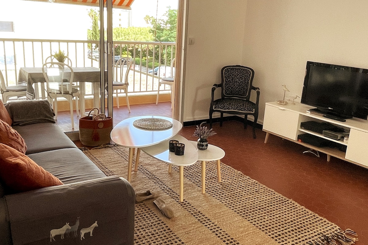 A living area is presented with a spacious couch and an accent chair. A coffee table is centrally positioned, with a decorative plant placed atop. Light enters through sliding glass doors that open to a balcony, while a dining table with chairs is visible in the background.