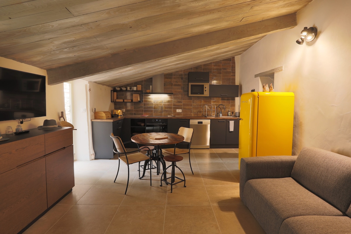 The kitchen and dining area is showcased with modern appliances, including a bright yellow refrigerator. A circular dining table with four chairs is positioned in the center, and a gray sofa sits nearby. Exposed wooden beams enhance the rustic charm of the space.