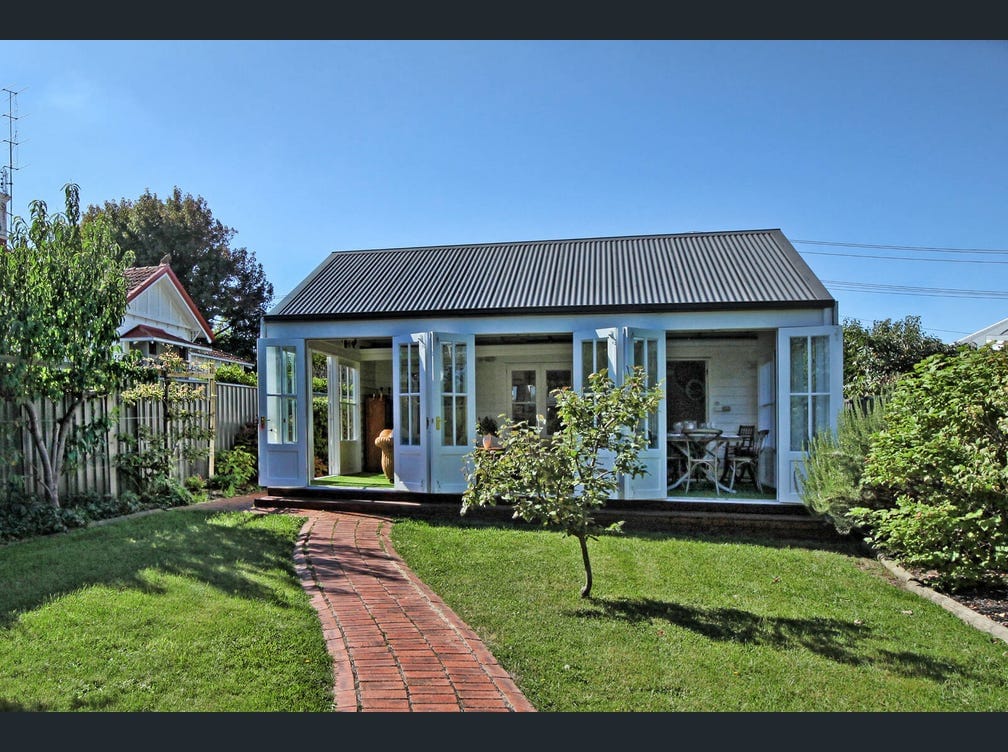 A charming cottage features large glass doors, creating an inviting connection to the outdoors. The surrounding garden showcases well-maintained grass and greenery, while a brick pathway leads to the entrance, enhancing accessibility and inviting exploration of the outdoor space.