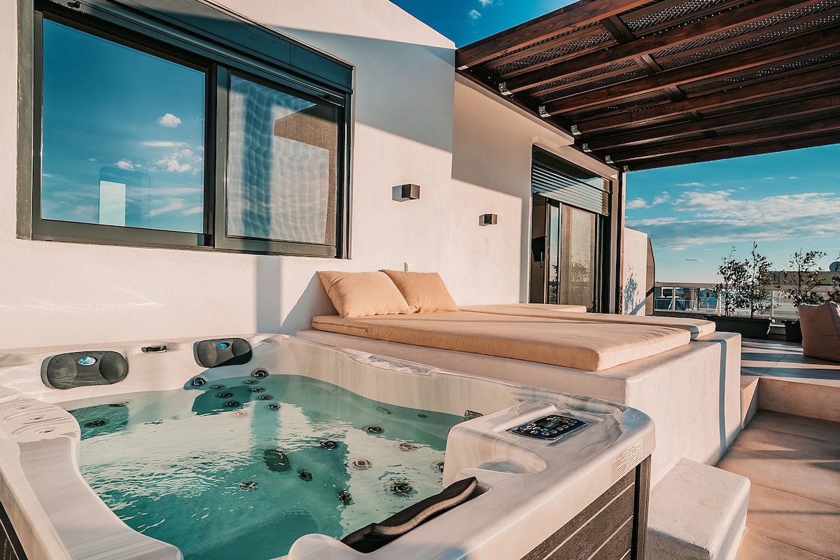 A private hot tub is set on a spacious terrace, surrounded by large windows that offer ample natural light. A comfortable sunbed is positioned alongside the tub, creating a relaxing space to enjoy the view. The tranquil setting invites moments of peace and leisure.