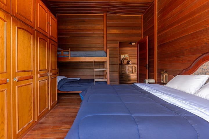 Útulná izba s drevenými stenami a nábytkom, manželskou posteľou a poschodovou posteľou, ideálna na ubytovanie rodín alebo skupín s pohodlím a rustikálnym šarmom.
