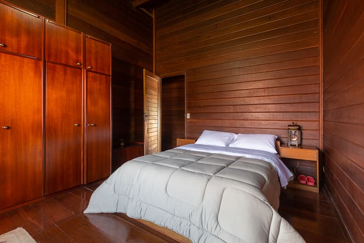 Útulná izba s drevenými obkladmi, manželskou posteľou s ľahkou posteľnou bielizňou a vstavanou skriňou. Útulné a pokojné prostredie, ideálne na chvíle odpočinku.