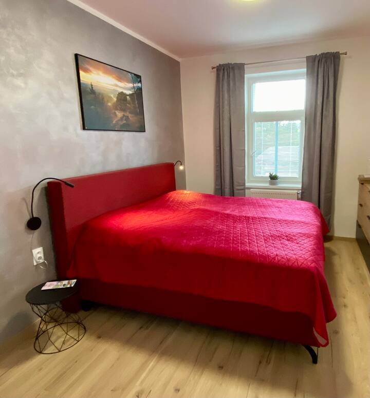 Просторен двоен кревет во спална соба со прозорец кон дворот.