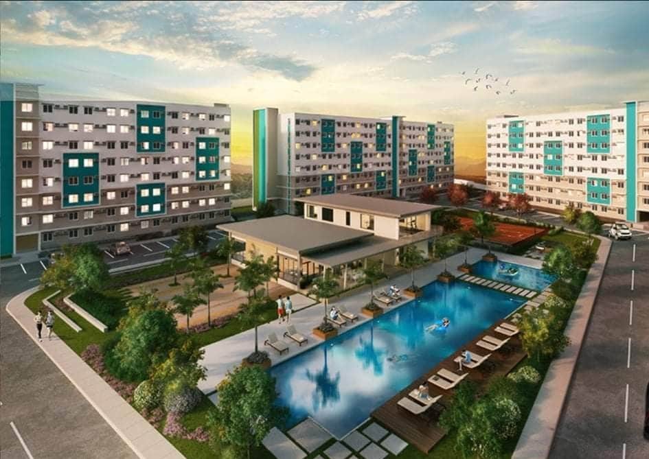 A modern residential complex is showcased, featuring multiple buildings with varying shades of blue and white. A sparkling swimming pool is framed by lounge chairs and palm trees, while landscaped areas provide greenery throughout the property.