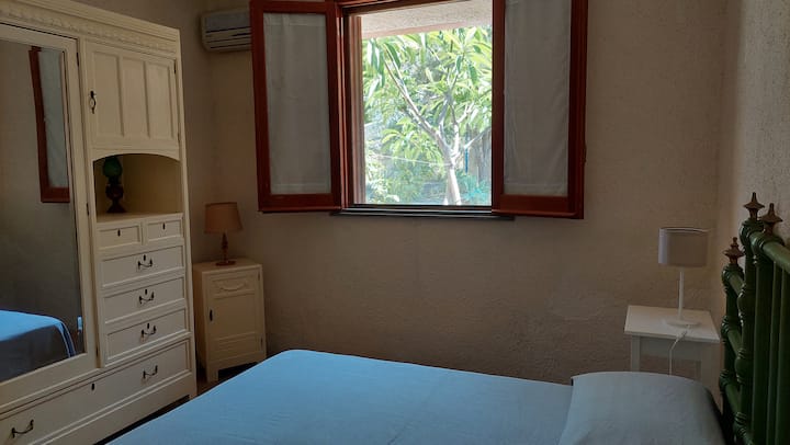 Camera con vista sul giardino mediterraneo, configurabile come matrimoniale o due letti singoli. Spalliera in ghisa, guardaroba Liberty dei primi Novecento e climatizzatore. La sera, il profumo del gelsomino siciliano entra dalla finestra.