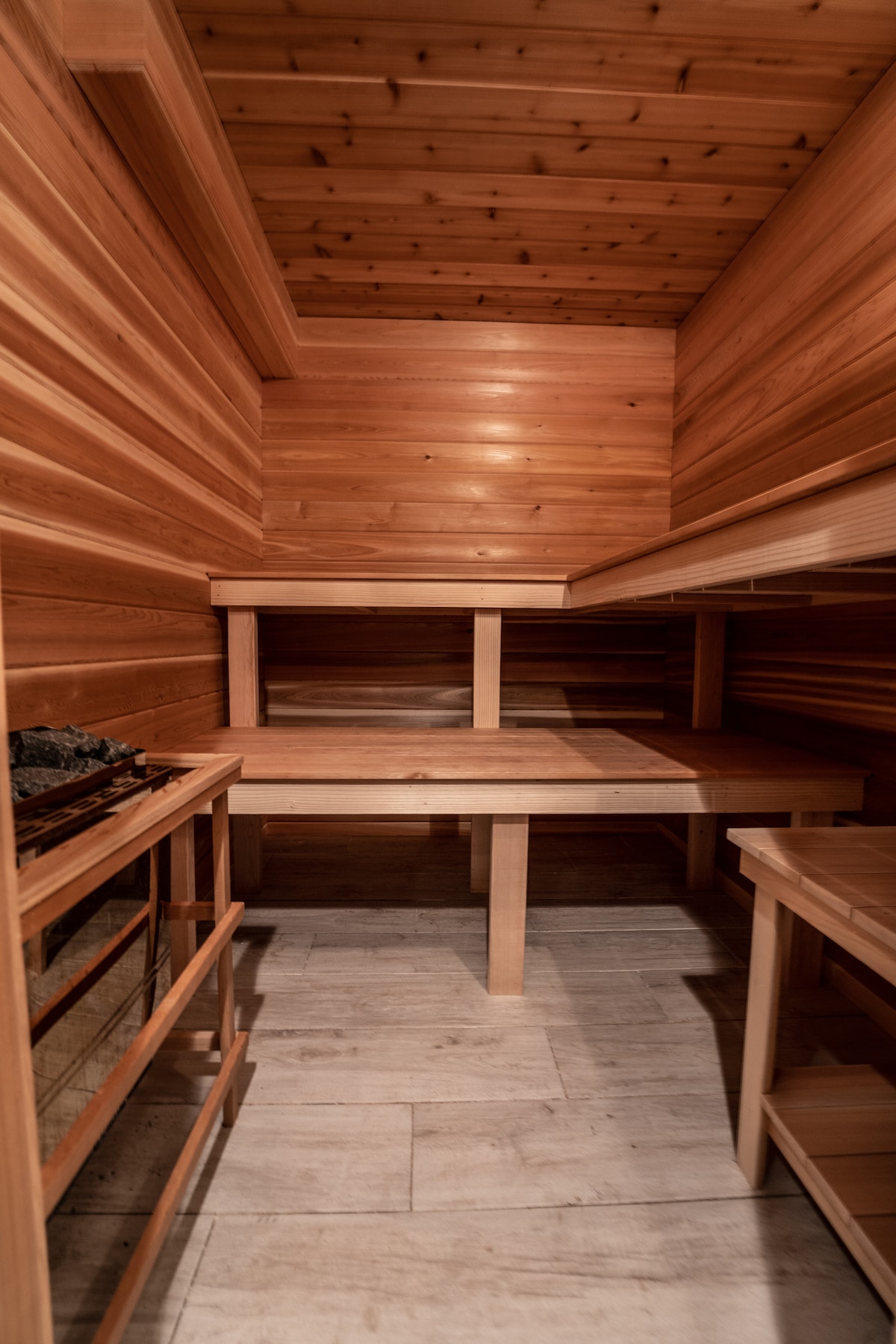 The interior of a sauna is shown, featuring warm wooden walls and benches. Subtle lighting enhances the natural wood grain, and a heater is positioned along one side. The clean lines and minimalist design create a tranquil environment for relaxation.