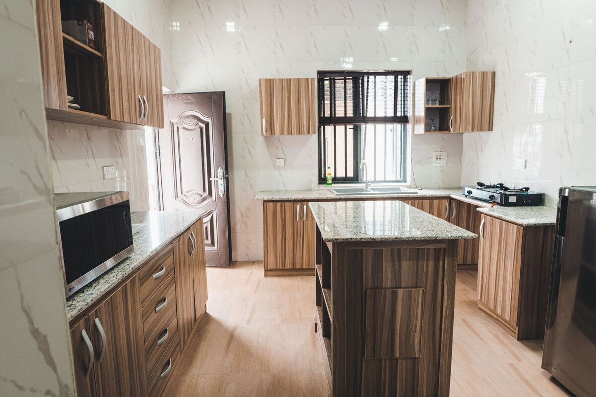 A modern kitchen features wooden cabinetry, complemented by a granite countertop. Natural light enters through a window, illuminating the space. Modern appliances, including a microwave and stove, are present, enhancing functionality in this inviting cooking area.