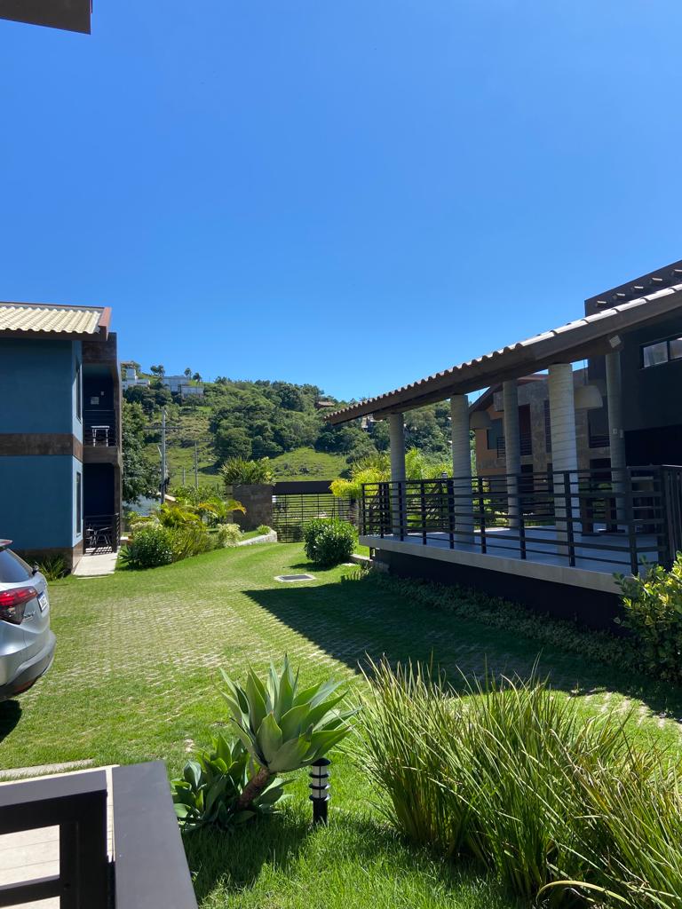 A well-maintained outdoor area is depicted, featuring a neatly landscaped garden with various green plants. The building architecture showcases wooden elements alongside modern features. A clear blue sky provides a bright backdrop, enhancing the serene atmosphere of the surroundings.