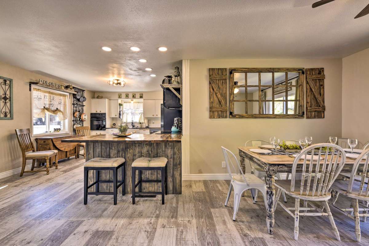 A modern kitchen and dining area showcase wood accents and a spacious island central to the layout. Barstools line one side of the island, while a dining table with mixed seating is set nearby. Natural light floods the space through large windows.