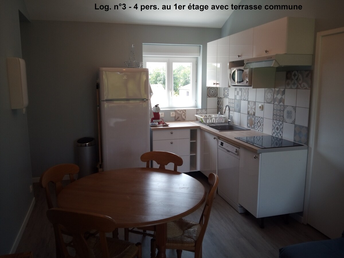 A modern kitchen area features white cabinetry with a decorative tile backsplash. A round wooden dining table is positioned nearby, surrounded by four chairs. Natural light enters through a window above the sink, illuminating the space. A full-size refrigerator is visible to the left.