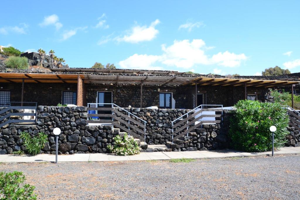 A stone structure with a rustic facade features multiple entrances, each with wooden awnings. Steps lead to the entrances, surrounded by greenery and pathways. The clear blue sky complements the natural stone, enhancing the authentic character of the building.