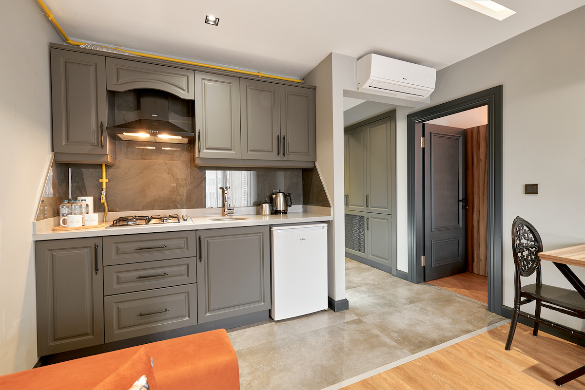 A stylish kitchen area features modern cabinetry and a gas stove. A compact refrigerator is positioned beside the counter. Natural light illuminates the space, which connects to an inviting dining area with a table and chairs. The interior combines functionality with a contemporary design.