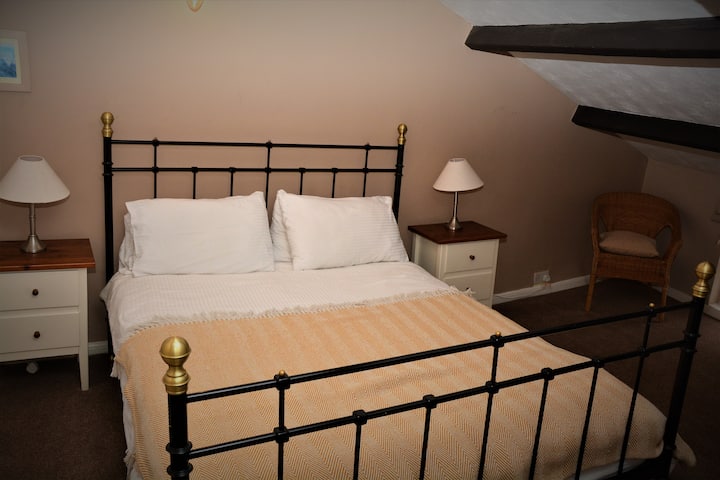 Dette er det største rum i huset og har igen fritliggende bjælker og skrånende lofter, hvilket gør det meget kort i den ene ende og meget højt i den anden . Der er en kingsize-seng.