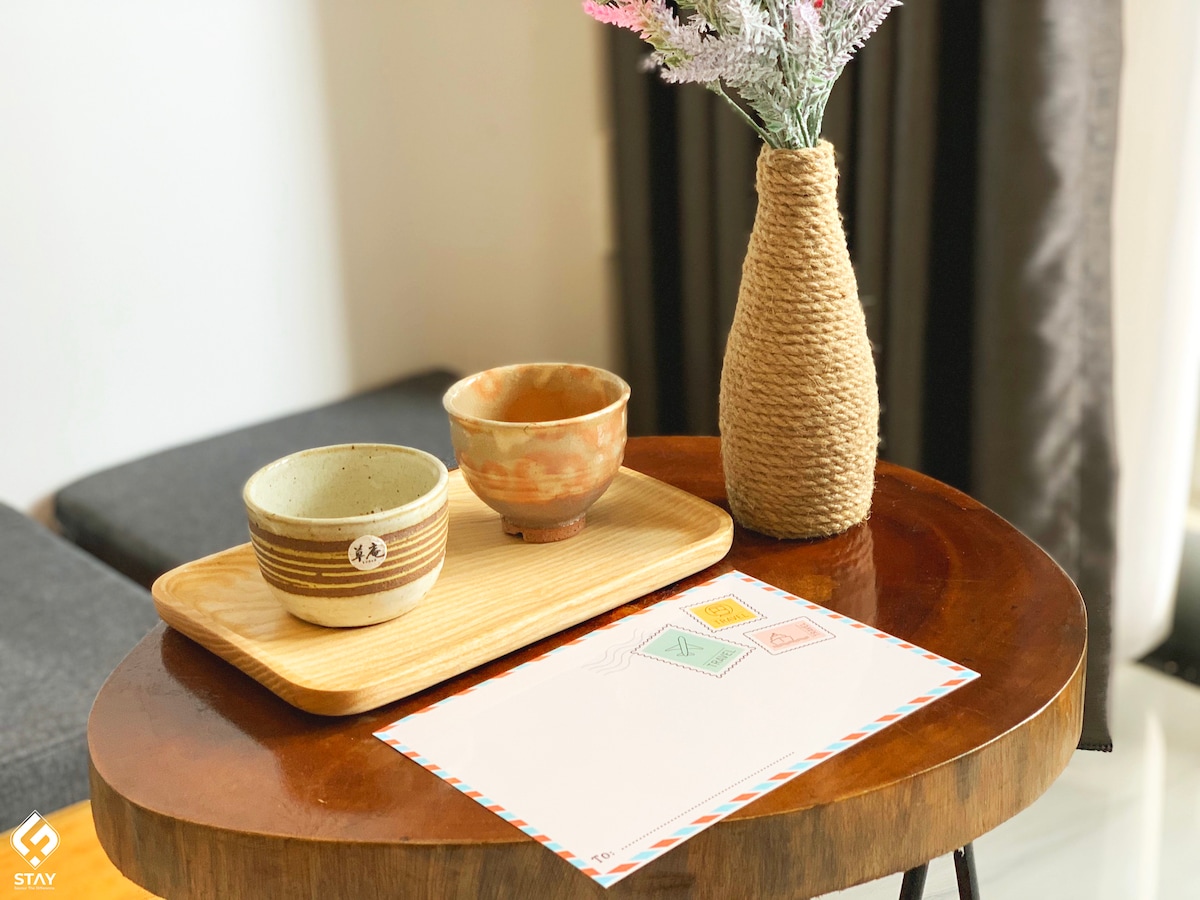 A wooden table showcases two bowls and a rectangular tray with a delicate floral arrangement in a textured vase. A notepad featuring colorful geometric designs is placed on the table, complementing the warm tones of the dishes.
