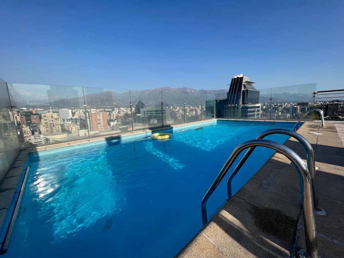 A rooftop pool area is highlighted, featuring clear blue water and a spacious deck. Glass barriers provide unobstructed views of the surrounding city and distant mountains. The sun creates reflections on the water, enhancing the inviting atmosphere of the space.