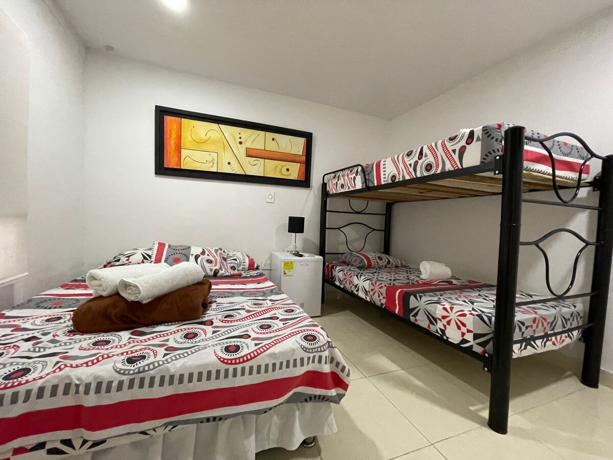 A sleeping area features a bunk bed with a lower double bed and an upper single bed, each adorned with a patterned bedspread. A small nightstand is positioned beside the beds, and towels are neatly arranged on the lower bed.