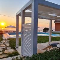 A sleek pergola is positioned near a tranquil pool, framed by well-maintained grass and a stone pathway. A vibrant sunset casts warm hues over the scene, while sun loungers and an umbrella are visible by the water's edge, enhancing the outdoor living space.