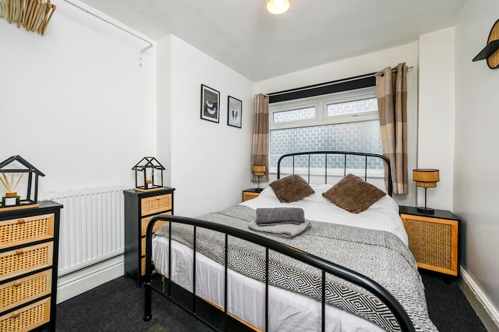 Уютна и привлекателна спалня с класическа метална рамка на леглото, свежо спално бельо и околно осветление. С акцент върху плетени детайли и монохромно изкуство, това е спокойно място за отдих за спокойни нощи. Идеалното място за презареждане по време на пътуванията ви.