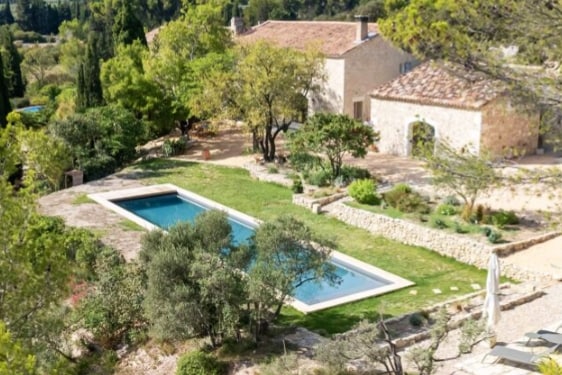 A serene outdoor area features a lengthy salt-water pool surrounded by lush greenery and carefully arranged stone pathways. The landscape includes various trees and plants, adding to the tranquil ambiance of the setting.