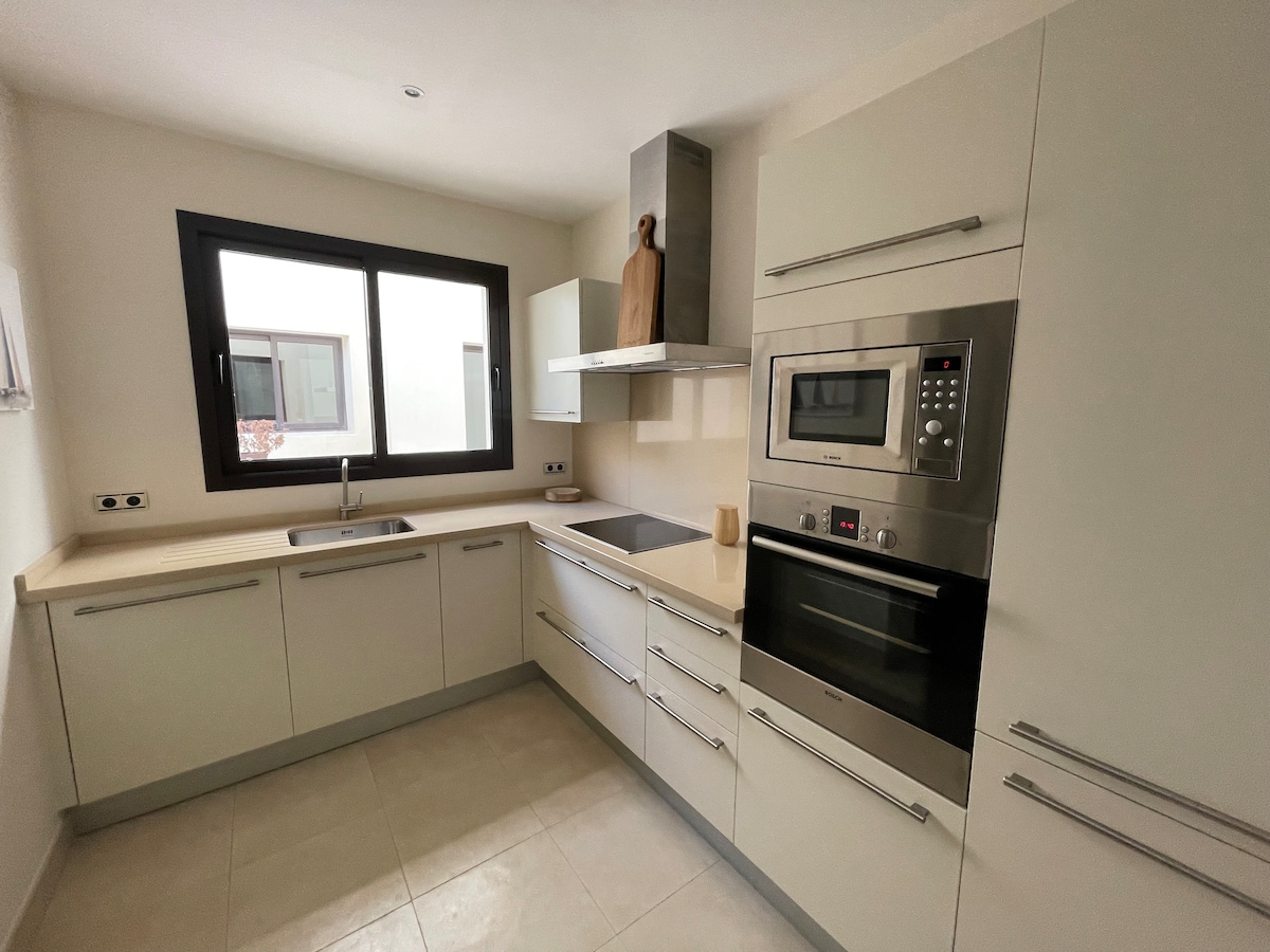 A contemporary kitchen features sleek cabinetry and modern appliances. Natural light enters through a large window above the sink. An integrated oven and a built-in microwave complement the stove, while ample counter space enhances functionality.