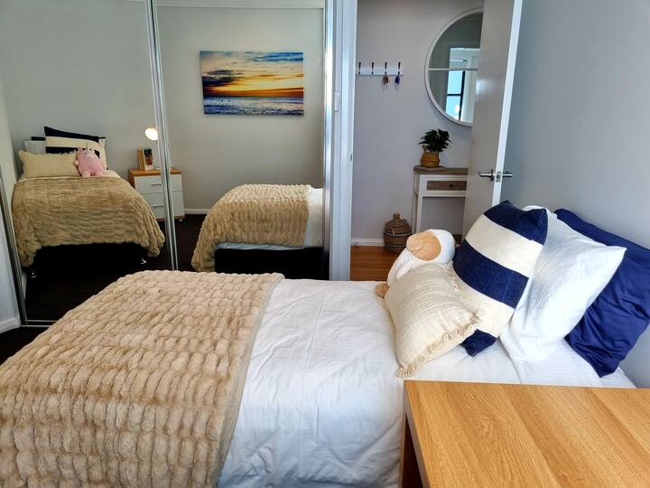 To the right of the entrance way, Bedroom 3 has 2 x single beds, work/study desk with plenty of natural light & mirror built in wardrobes. Up the top of the wardrobes is a portable cot, baby bath & a highchair.