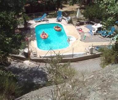 A private swimming pool is surrounded by loungers and shaded areas. The pool area includes two kayaks floating on the water. Lush greenery frames the setting, enhancing the sense of seclusion. A sun umbrella provides shade nearby, contributing to a relaxing outdoor environment.