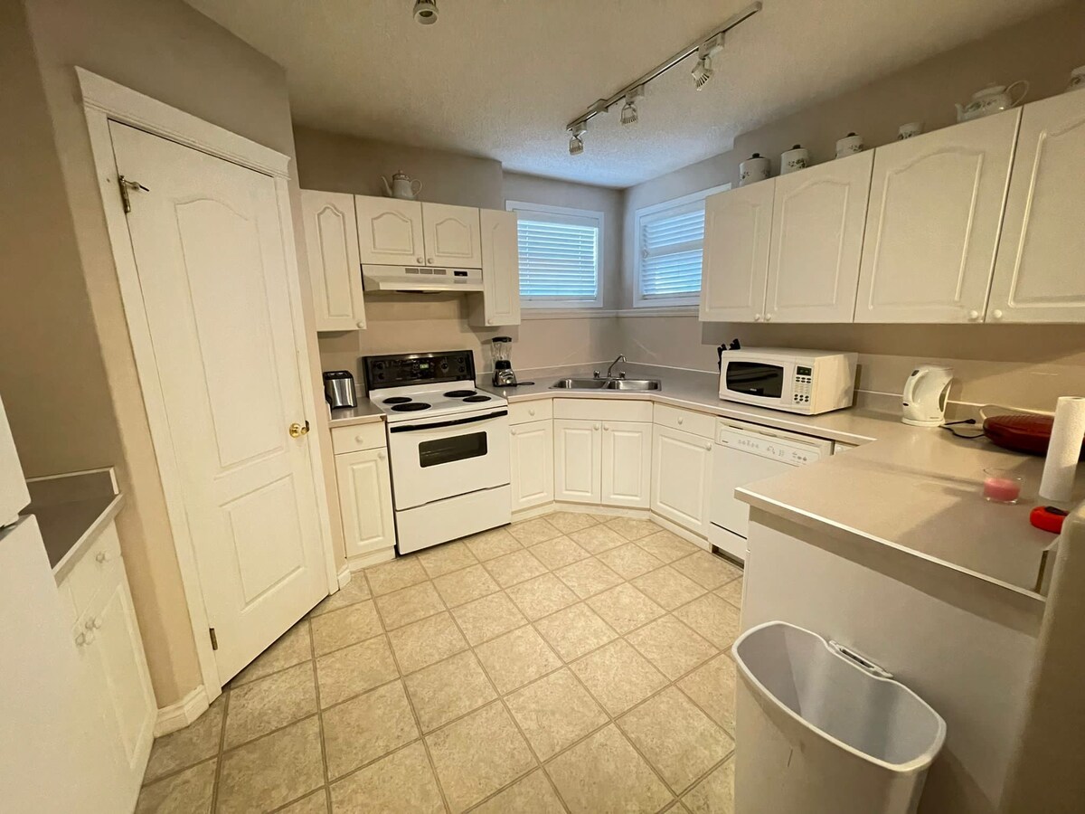 The kitchen is equipped with white cabinetry, featuring a stove, oven, and microwave. A refrigerator and dishwasher are also present, along with essential appliances. Natural light enters through two windows, and the tiled floor adds a practical touch to the space.