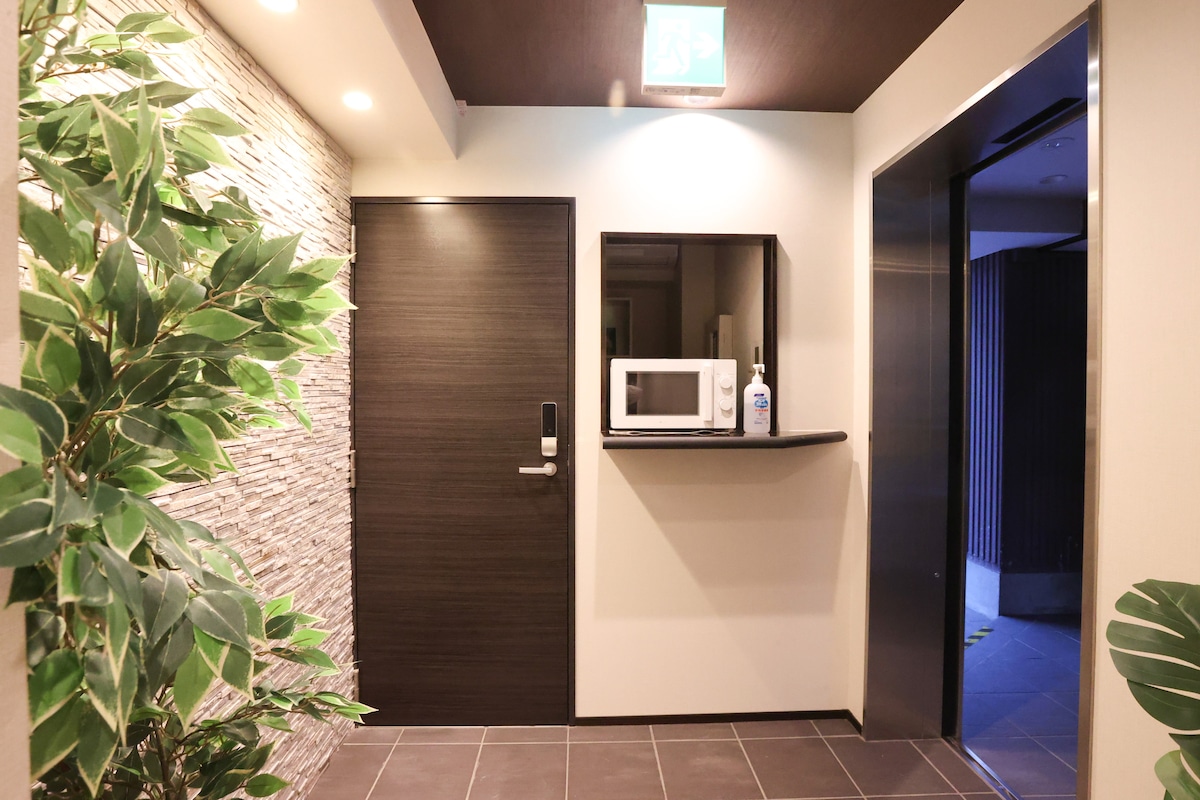 The entrance area features a combination of modern design elements, including a dark door and a sleek wall-mounted microwave. A stone accent wall adds texture, while potted greenery enhances the welcoming ambiance. Soft lighting illuminates the space, contributing to a cozy atmosphere.