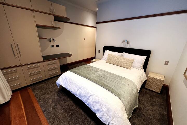 EL DORMITORIO DE INVITADOS 2 cuenta con un baño privado, ropa de cama de calidad, una alfombra de felpa, un armario y un escritorio/tocador. Las puertas dobles conducen a una terraza cubierta y a vistas sobre la terraza trasera (juego de ajedrez gigante, mesa de comedor y anillo de baloncesto).