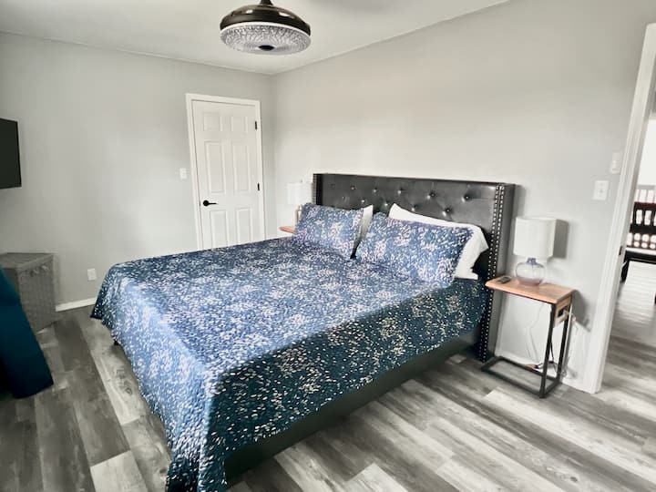 ห้องนอน 2 จาก 2 บนชั้นหลักพร้อมเตียงคิงไซส์ที่สะดวกสบายทีวีและหน้าต่างที่มองเห็นสวนหลังบ้านและฟาร์มใกล้เคียงในระยะไกล