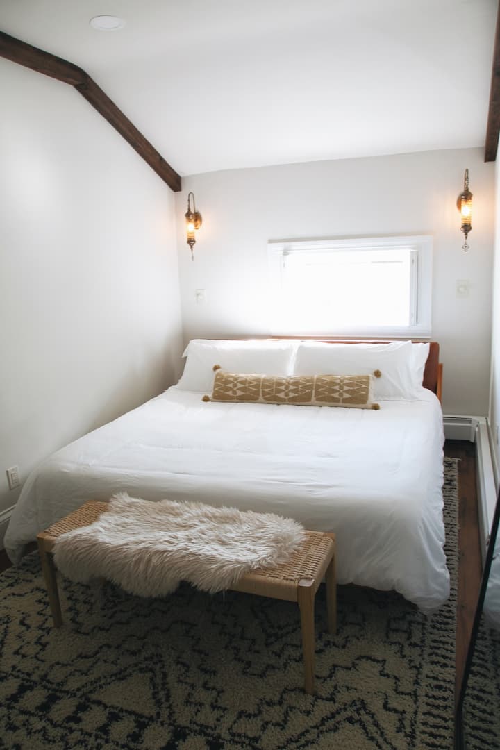 This cozy bedroom has a special ambiance. A king size bed from CB2 with luxurious bedding is sat under a window with historic 1830s shutters and hardware. Handmade moroccan sconces radiate warmth and intimacy.