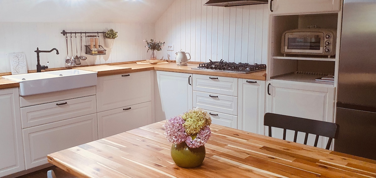 The kitchen features wooden countertops and a spacious sink, with ample storage cabinets beneath. A modern stove is positioned against the wall, while the dining area includes a wooden table accompanied by black chairs. A vase with flowers adds a touch of color to the setting.