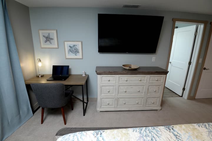 Upstairs features primary bedroom with king sized bed, 60 inch TV, double closets, dresser, desk, balcony and en suite bathroom. 