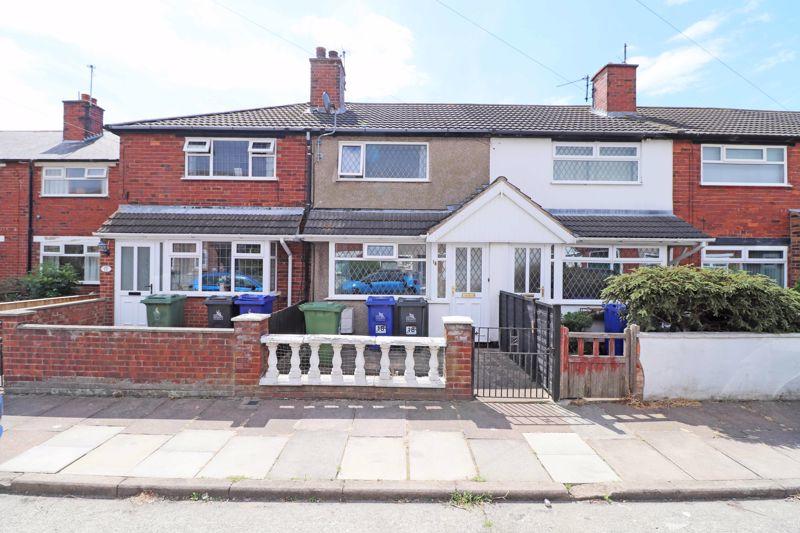 A row of terraced houses displays a combination of red brick and light-colored facades. A white front porch is visible, framed by two large windows. Green and blue recycling bins are placed along the pathway, leading to a small gated entrance surrounded by a low wall.