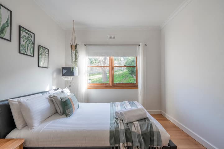 The second bedroom features a queen-size bed complete with bedside tables and lamps, with leafy views looking out to the backyard.

