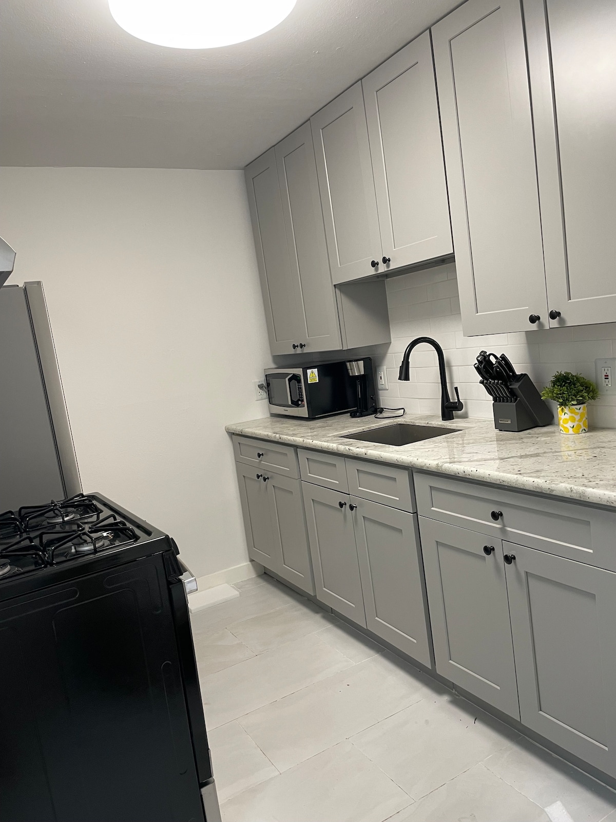 The kitchen features modern gray cabinetry with sleek hardware, a stainless steel refrigerator, and a black gas stove. A countertop made of light-colored stone provides workspace. Essential appliances include a microwave and a black faucet atop a deep sink, enhancing the kitchen's functionality.