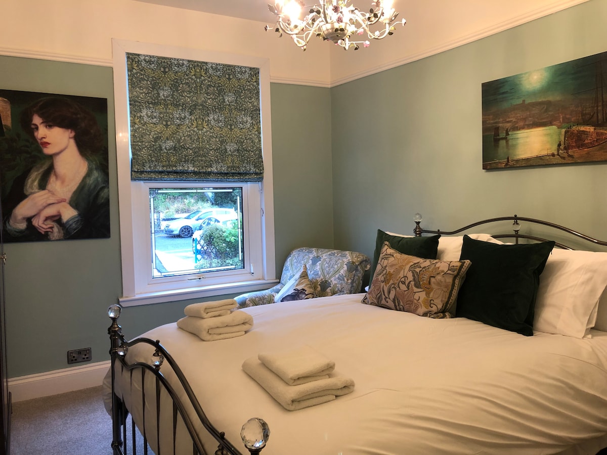 ห้องนอนสีเขียวชั้นแรกสไตล์วิคตอเรียที่น่าทึ่ง ด้วยมู่ลี่วิลเลียมมอร์ริสโรมันภาพพิมพ์ Pre-Raphaelite และ Grimshaw พัดลมไดร์เป่าผมและที่วางสัมภาระรวมถึงหัวหุ่นแปลกๆและโคมไฟระย้าดอกไม้ที่สวยงาม ทุกอย่างมีคุณภาพดีเยี่ยม 