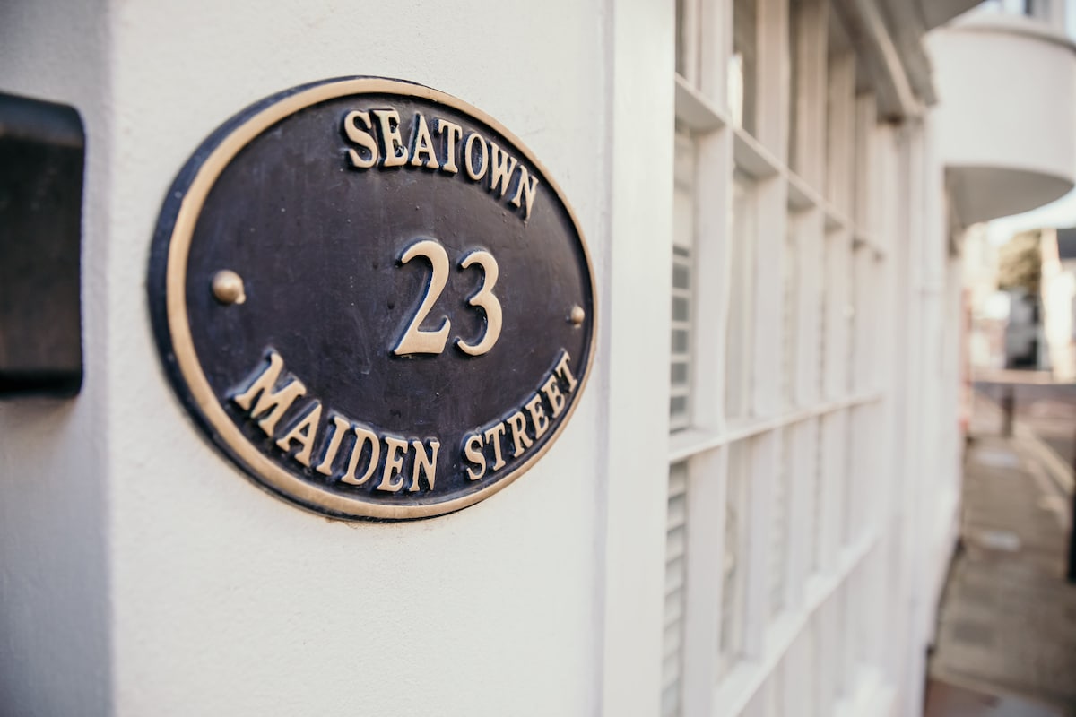 The property’s entrance is marked by an elegant black plaque with gold lettering, prominently displaying the address '23 Seatown Maiden Street.' Sunlight softly reflects off the surrounding white wall, creating a welcoming impression.
