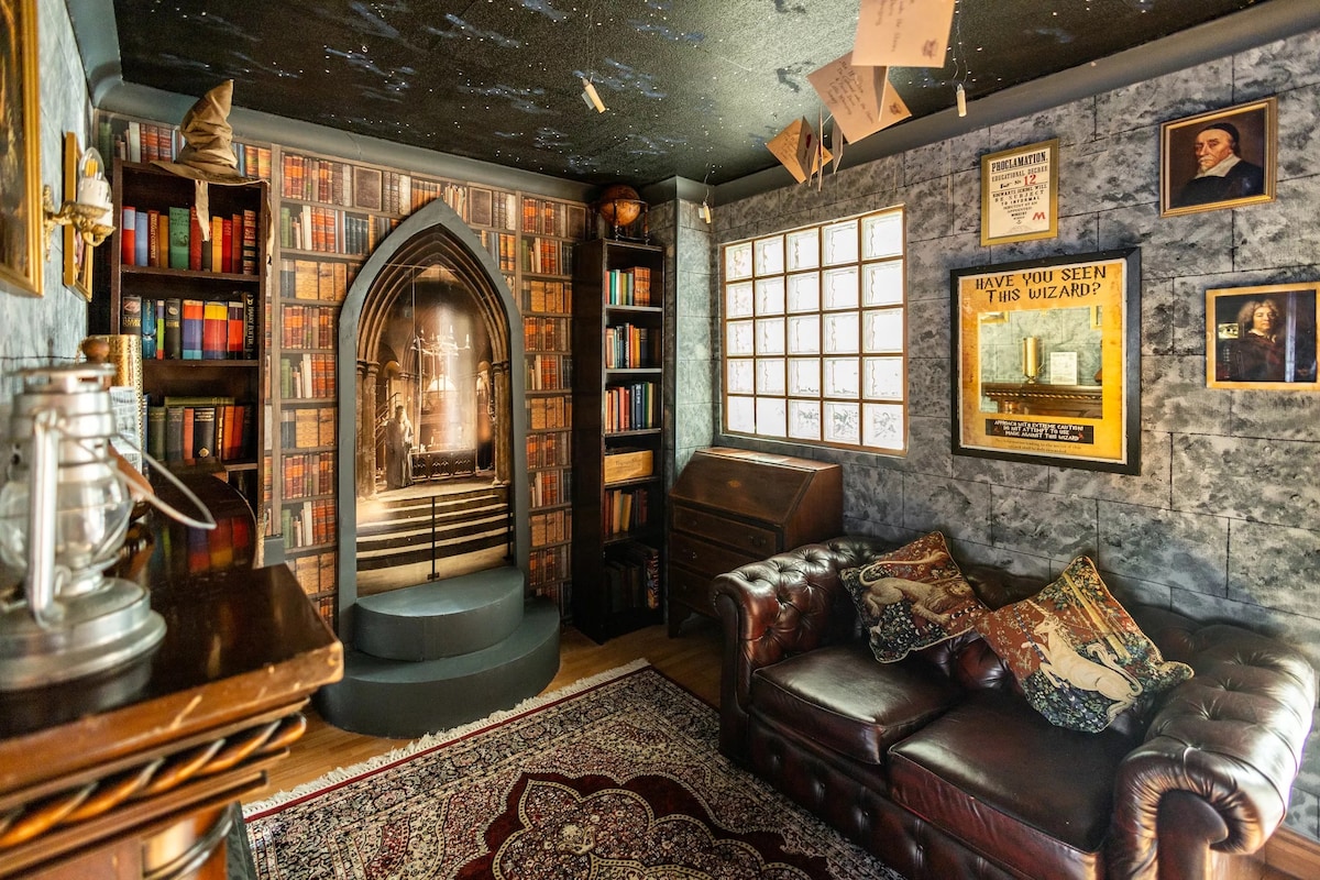 A themed reading nook features a dark, textured wall with an arched bookshelf filled with vintage-looking books. A cozy leather sofa is adorned with patterned cushions, while a vintage-style lamp stands nearby. An intriguing backdrop displays a staircase illuminated by soft light, enhancing the magical atmosphere.