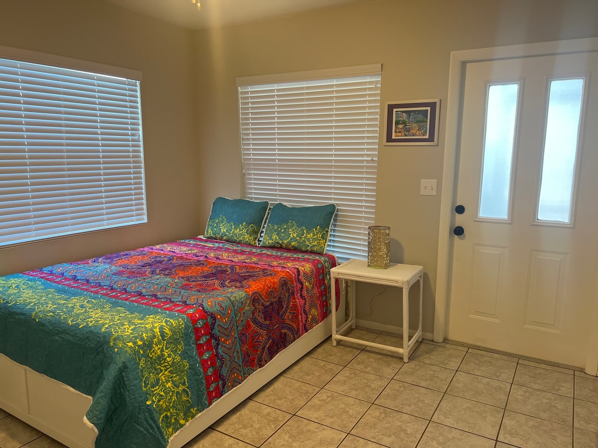 Брачна спална соба со врата до параван во поплочен двор со 2 стола за лулање и врата до двор. И близнак тркалце. 