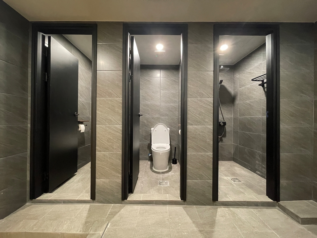 Two separate restrooms are visible, featuring modern fixtures and minimalistic design. Each restroom includes a toilet with sleek tiles and is well-lit, creating a functional space. Hooks for personal items can also be found in one restroom, ensuring convenience.