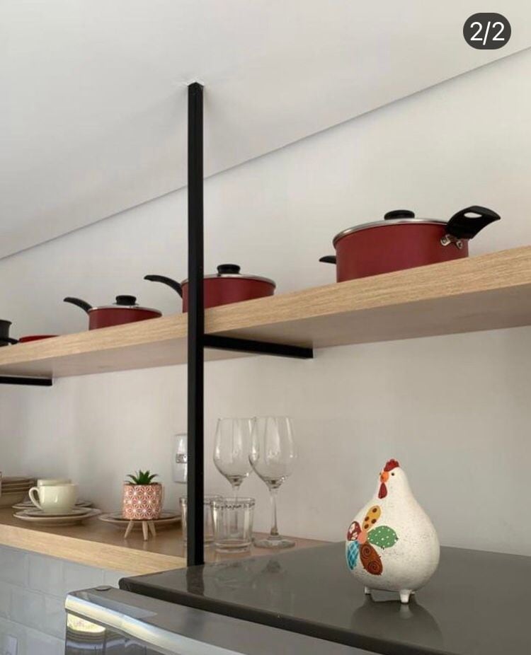 Open shelves display a collection of red cooking pots along with a decorative chicken figurine. Glassware and additional kitchen items are neatly arranged, complemented by a small potted plant. A sleek refrigerator is visible below, showcasing a modern kitchen design.