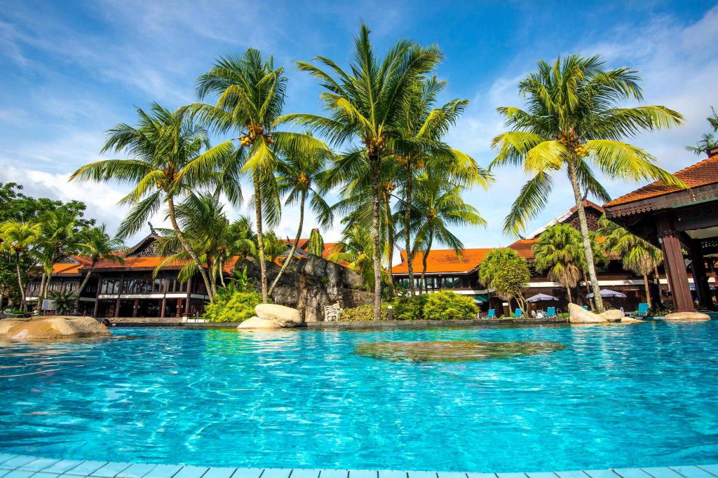 A tranquil pool is surrounded by tall palm trees, reflecting vibrant blue skies. The lush tropical landscape contributes to a serene atmosphere, while a wooden structure with a traditional design is visible in the background.